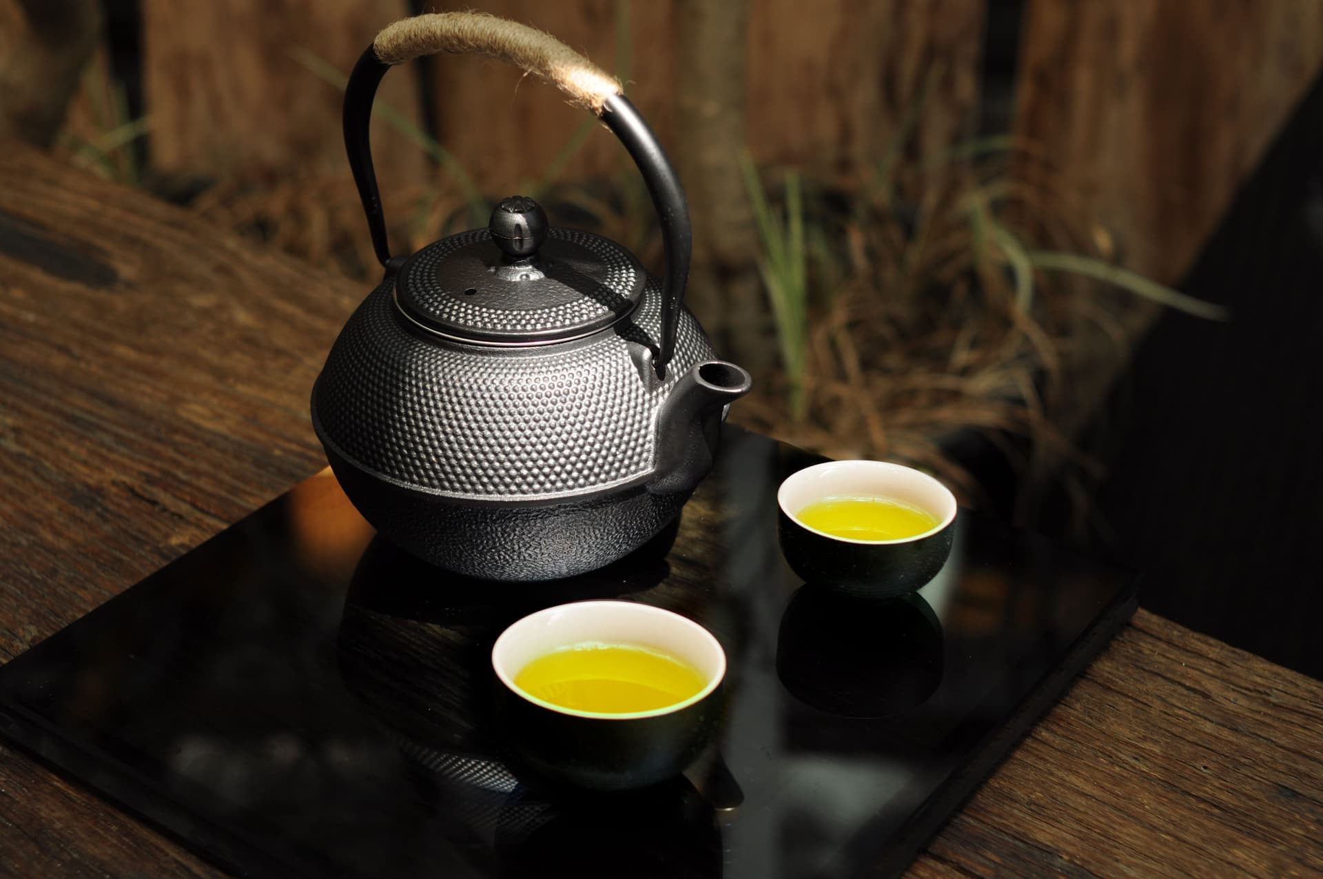 A cast iron teapot on a wooden surface beside a small cup